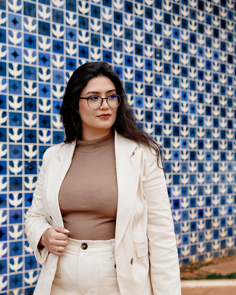 Eduarda Dornelles de blazer claro, em frente a um painel de azulejos azuis e brancos